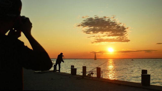 A guy takes a photo from a fisherman at  the sunset on lake Balaton
