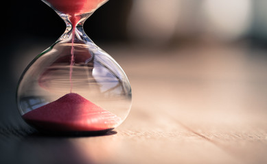 Red sand running through the bulbs of an hourglass measuring the passing time in a countdown to a deadline, on a bright background with copy space.