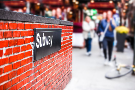 New York City Street Corner Subway Entrance With Sign On Brick Wall And Blur Of Women Walking In The Background