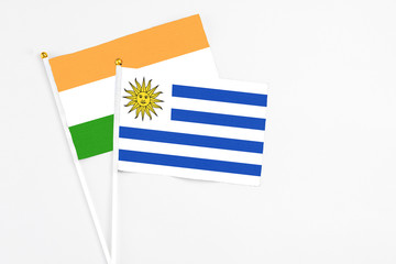 Uruguay and India stick flags on white background. High quality fabric, miniature national flag. Peaceful global concept.White floor for copy space.