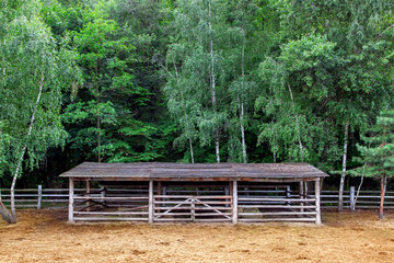 farm shelter pasture for cloven-hoofed animals with a barn canopy for animals, a place for pasture  with dry hay and green trees without animals nobody, front view.