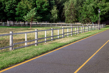 asphalt road with yellow markings on the side a wooden fence for pasture, without animals there is...