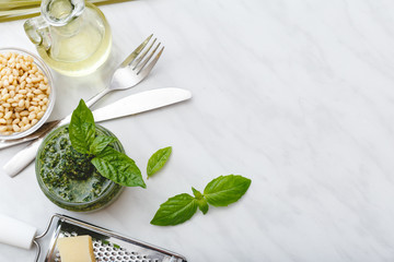 Pesto sauce with cutlery and ingredients: pine nuts, basil, olive oil, parmesan over white marble background. Top view, flat lay with copy space for text.Italian pesto sauce in for pasta, spaghetti