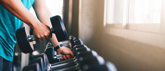 hands of man lifting dumbbells on rack in gym or fitness