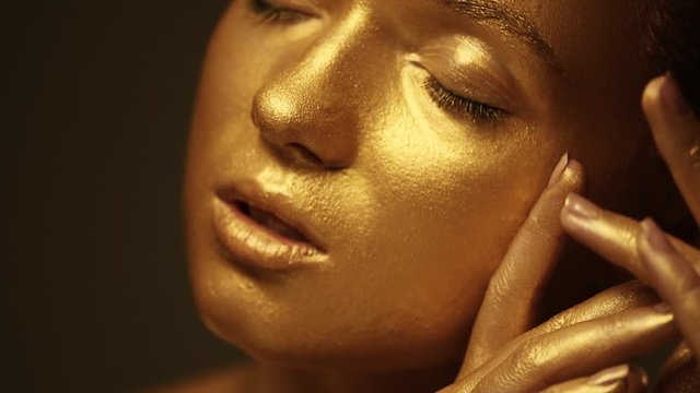 Fashion model woman in golden bright sparkles posing in studio, portrait of beautiful sexy girl with golden skin. Glitter gold metallic shine makeup. Slow motion 4K UHD video footage. 3840X2160