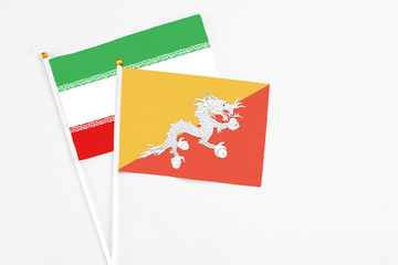 Bhutan and Iran stick flags on white background. High quality fabric, miniature national flag. Peaceful global concept.White floor for copy space.