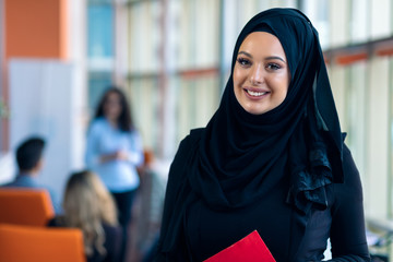 Cheerful woman in the office, holding folder with documents and giving a bright smile. Muslim women...