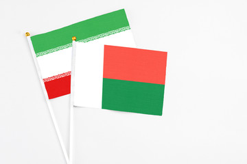 Madagascar and Iran stick flags on white background. High quality fabric, miniature national flag. Peaceful global concept.White floor for copy space.