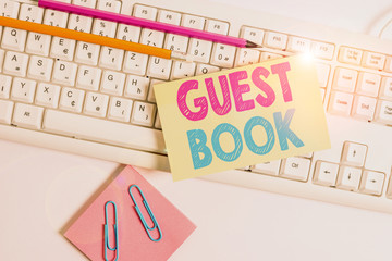 Conceptual hand writing showing Guest Book. Concept meaning electronic means for a visitor to acknowledge a visit to a site White keyboard with note paper and clips on white background