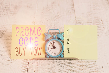 Writing note showing Promo Code Buy Now. Business concept for Giving great discount by entering special words Mini blue alarm clock standing above buffer wire between two paper