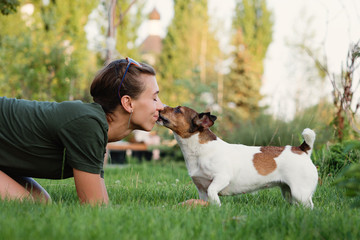 Dog kissing her owner outside. Lovely woman walking with her Jack Russell Terrier in summer...
