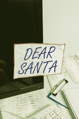Text sign showing Dear Santa. Business photo text letter intended for Santa Claus written by kids during Christmas Note paper taped to black computer screen near keyboard and stationary