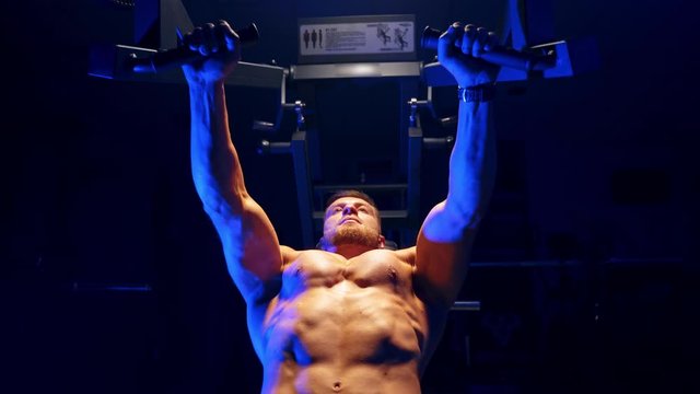 Handsome young man doing bench press workout in gym. Blue light filter. Strong abs. Heavy lift. Video from below.