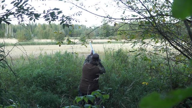 Man aims and fires a double barrel shotgun up in the air at game birds
