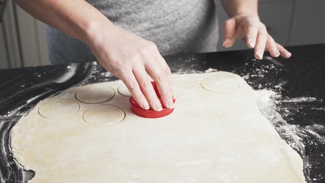 Lady using a cookie cutter to cut shapes of dough rolled out on her counter. Woman making mincemeat pie cuts dough to make pastry shells. Holiday baking and cooking concept. PAN LEFT.