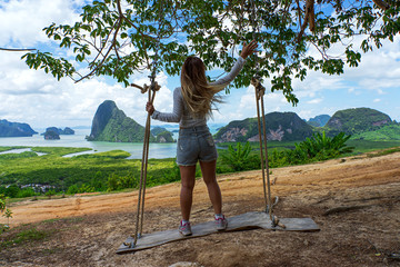 Asian woman standing on swing with islands and sea background