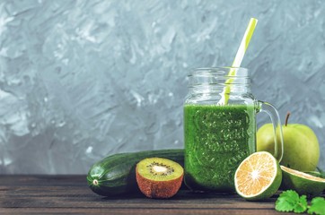 healthy green smoothie with ingredients on a wooden table: apple, kiwi, lime, spinach, mint, avocado, cucumber