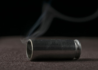The shotgun cartridge lies on the floor or on the road. There is smoke from the cartridge case, she...