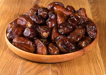 Dried dates on a wooden plate on a wooden table