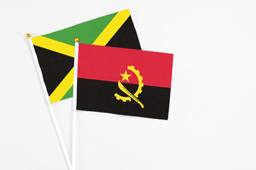 Angola and Jamaica stick flags on white background. High quality fabric, miniature national flag. Peaceful global concept.White floor for copy space.