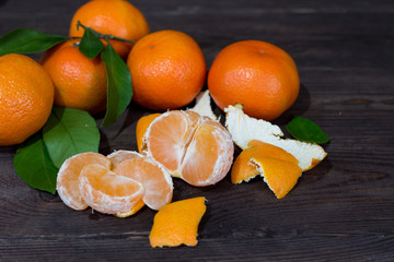 Fresh orange tangerines and slices of peeled fruit on a dark wooden table. The concept of a healthy diet and vegetarianism.