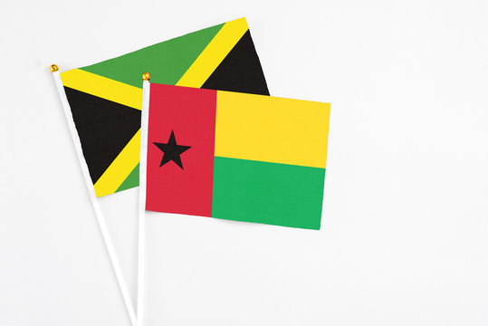 Guinea Bissau and Jamaica stick flags on white background. High quality fabric, miniature national flag. Peaceful global concept.White floor for copy space.