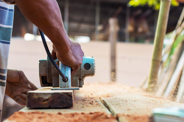 The carpenter's hands use a planer on the floor and create dust from work.