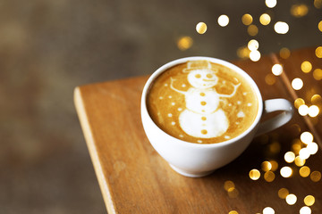 Tasty cappuccino with Christmas snowman art with some blurred lights.
