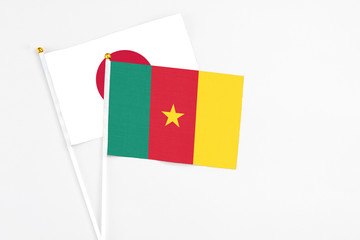 Cameroon and Japan stick flags on white background. High quality fabric, miniature national flag. Peaceful global concept.White floor for copy space.