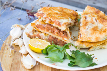 Lobiani - traditional baked Georgian pie with lobio beans and filo puff pastry. On plate with lemon slice, green rucola leaves and garlic. Homemade.