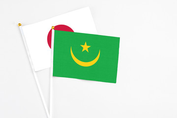 Mauritania and Japan stick flags on white background. High quality fabric, miniature national flag. Peaceful global concept.White floor for copy space.