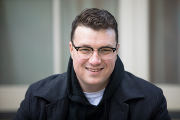 Obraz premium A caucasian male wearing a black hoodie sweater and glasses poses in a garden while surrounded by fall foliage on a cold afternoon.
