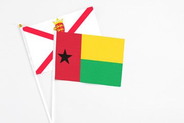 Guinea Bissau and Jersey stick flags on white background. High quality fabric, miniature national flag. Peaceful global concept.White floor for copy space.