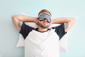 Sleeping young man with pillow on color background