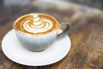 One cup of cappuccino with beautiful latte art on wooden brown background.