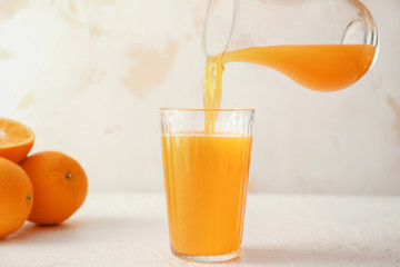 Pouring of fresh orange juice from jug into glass on table