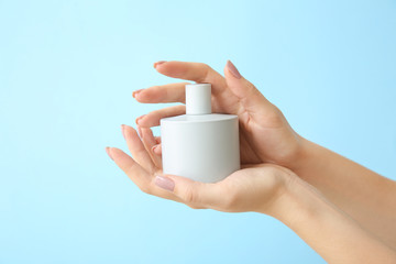 Female hands with bottle of perfume on color background