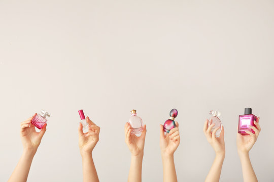 Female hands with different perfume bottles on grey background