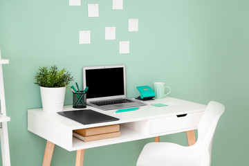 Comfortable workplace with modern laptop near color wall