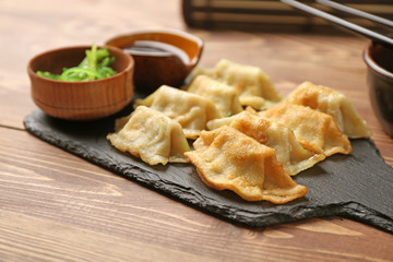 Slate plate with tasty Japanese gyoza on wooden table