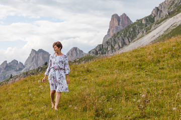 Naklejka na ściany i meble Girl in a dress on a background of mountains. Mountain valley of the Alps, Dolomites. Summer sunny day