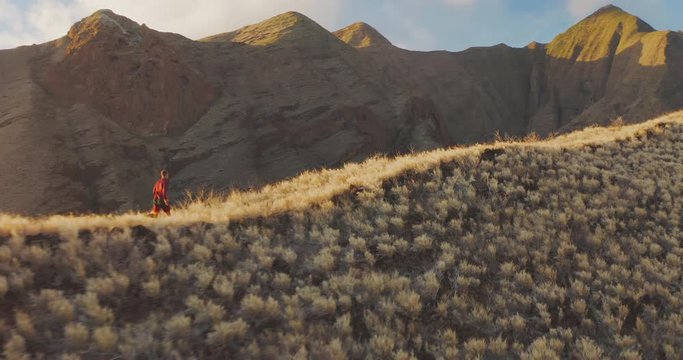 Aerial view of a fit adventurous man running on a golden mountain ridge at sunset in the great outdoors on the weekend, amazing trail running moments, achieving his fitness goals in the mountains
