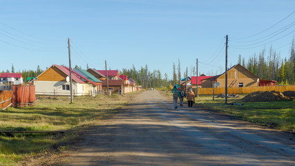 Yakut family of men with a woman and a young girl with a backpack is in the shade on the road in...
