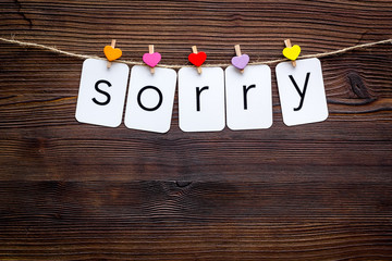 Apologise concept. Cute heart icons garland with text sorry on dark wooden background top view copy space