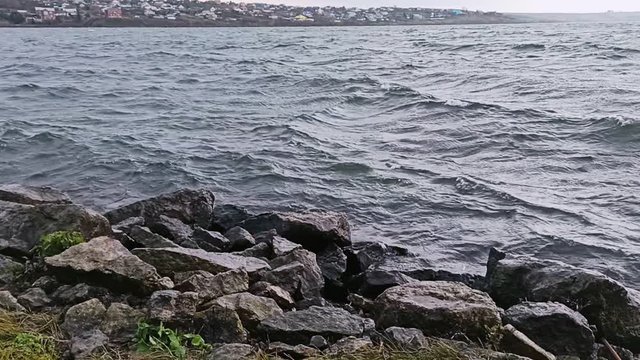 Waves of the river hit the stones on a cloudy day. Spray in the wind