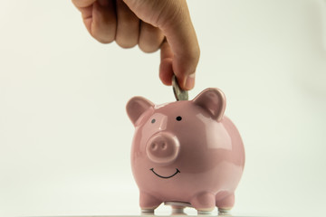 Adult hand insert coin into pink piggy bank with white background. Saving purpose concept.