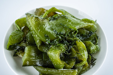 Fresh green salted sea cabbage stems on a saucer on a white background