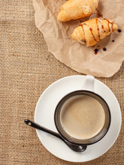 Cup of black coffee with fresh croissants on wrapping paper