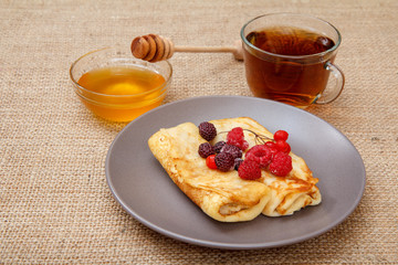 Homemade pancakes filled with cottage cheese, honey in a bowl and a cup of tea