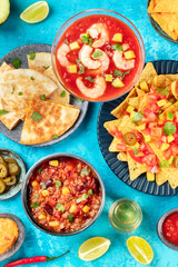 Mexican food, many dishes of the cuisine of Mexico, flat lay top-down shot from on a vibrant blue background. Shrimp cocktail, nachos, tequila, chili con carne, quesadillas